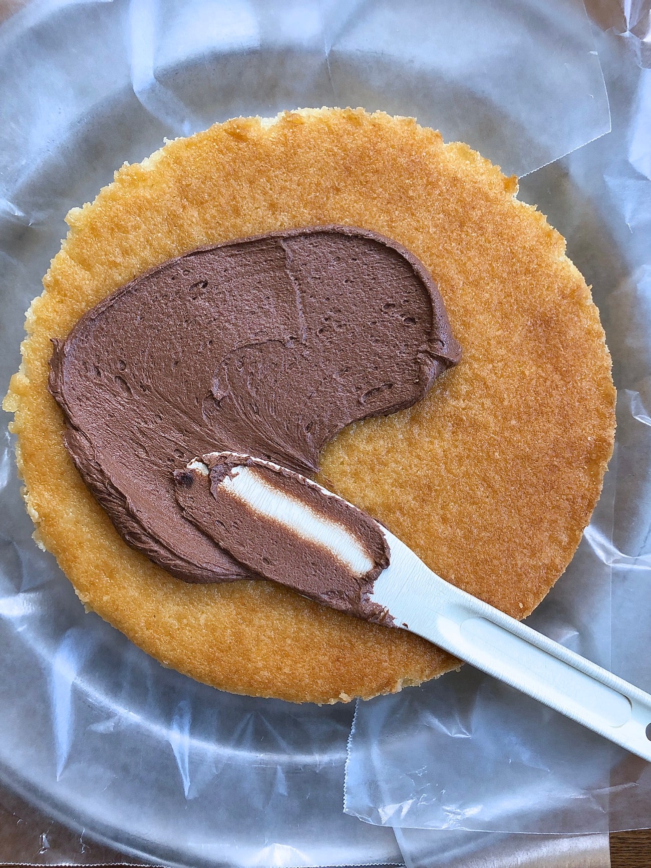 Chocolate frosting being spread onto a round layer of yellow cake.